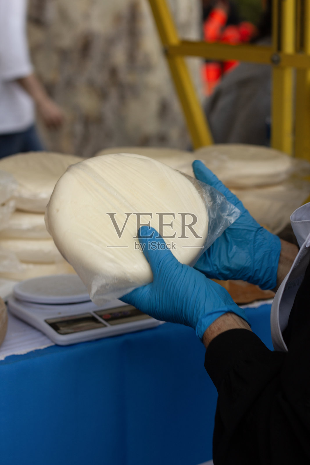女性戴着蓝色手套的手。女人手中拿着新鲜的苏卢古尼奶酪轮。照片摄影图片