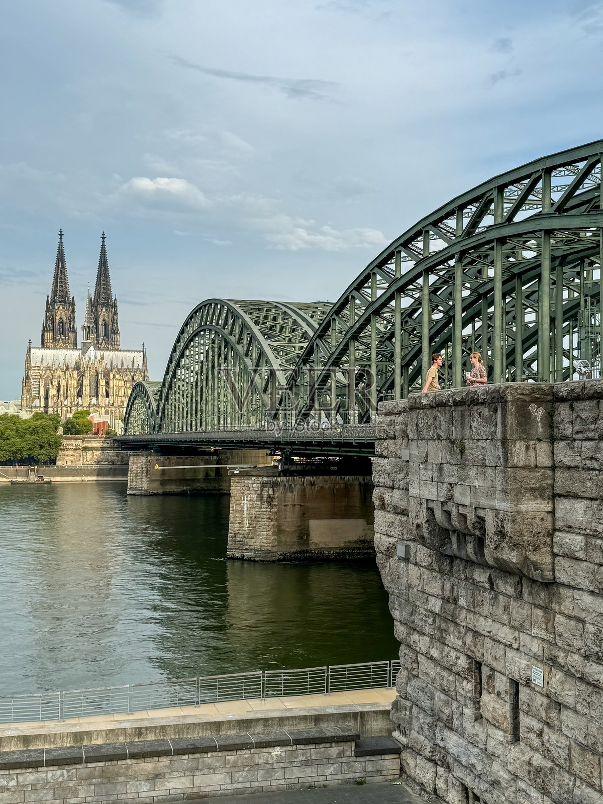 一位母亲和儿子在德国科隆欣赏霍亨索伦桥和大教堂的日出美景，天空布满蓝色云彩。照片摄影图片