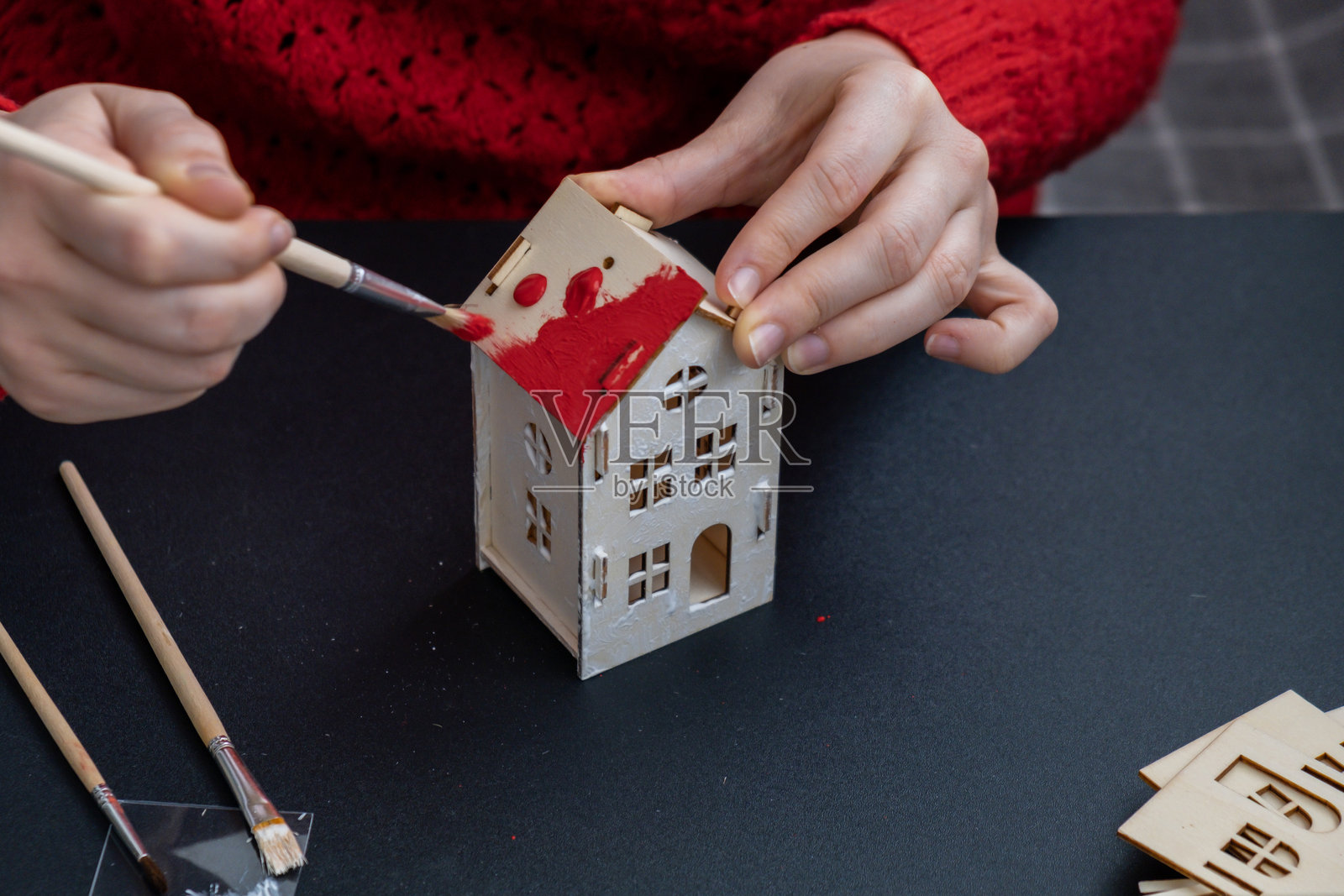 准备圣诞节和新年除夕的过程。一位身穿红色毛衣的女士正在绘制3D木制房屋DIY。负责任的生态零浪费手工装饰。儿童爱好活动照片摄影图片