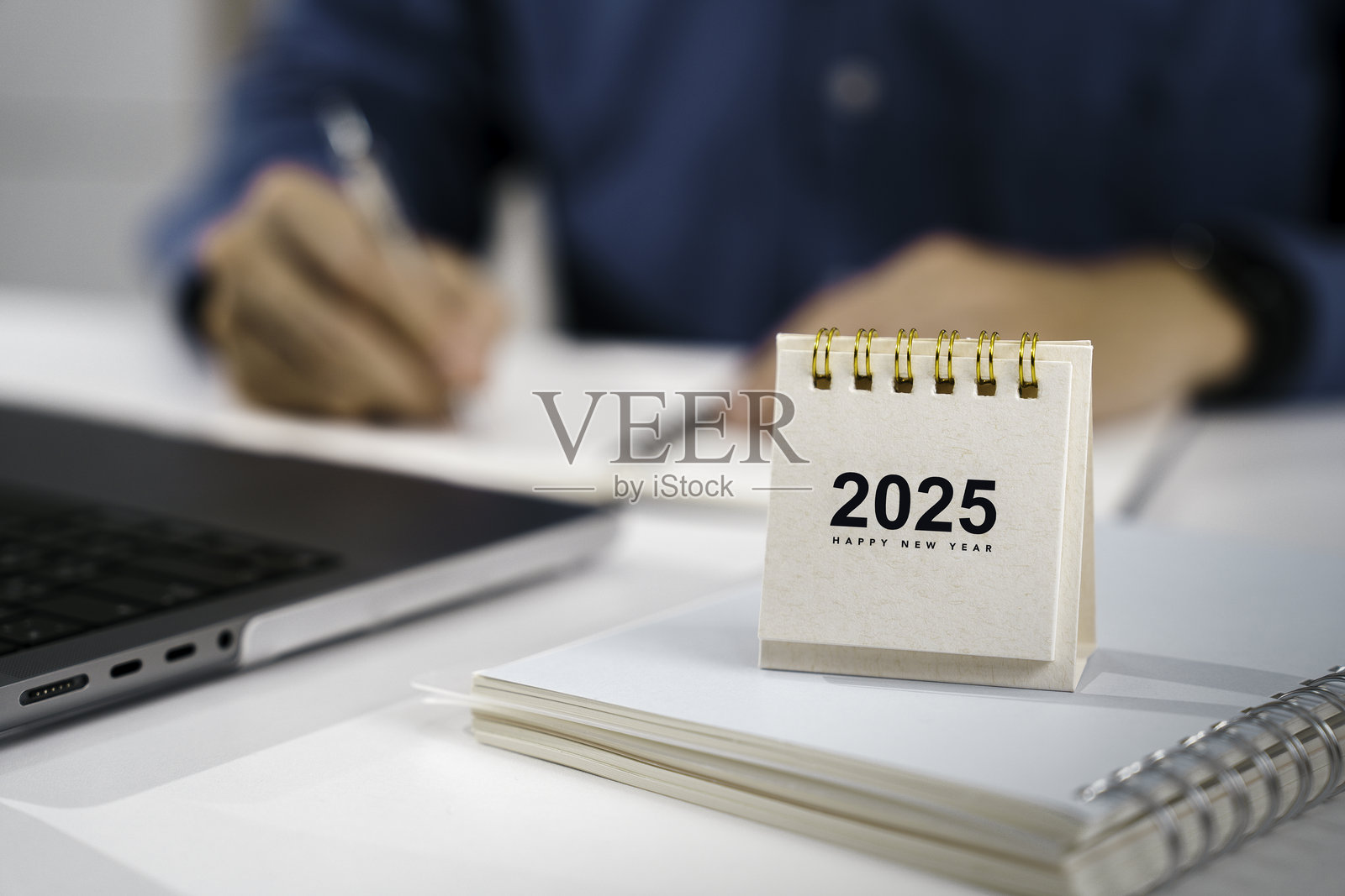 2025年新年快乐日历放在桌子上，商人正在笔记本上写下新年计划，准备开始工作。新年倒计时。目标计划、行动、使命和财务概念。照片摄影图片