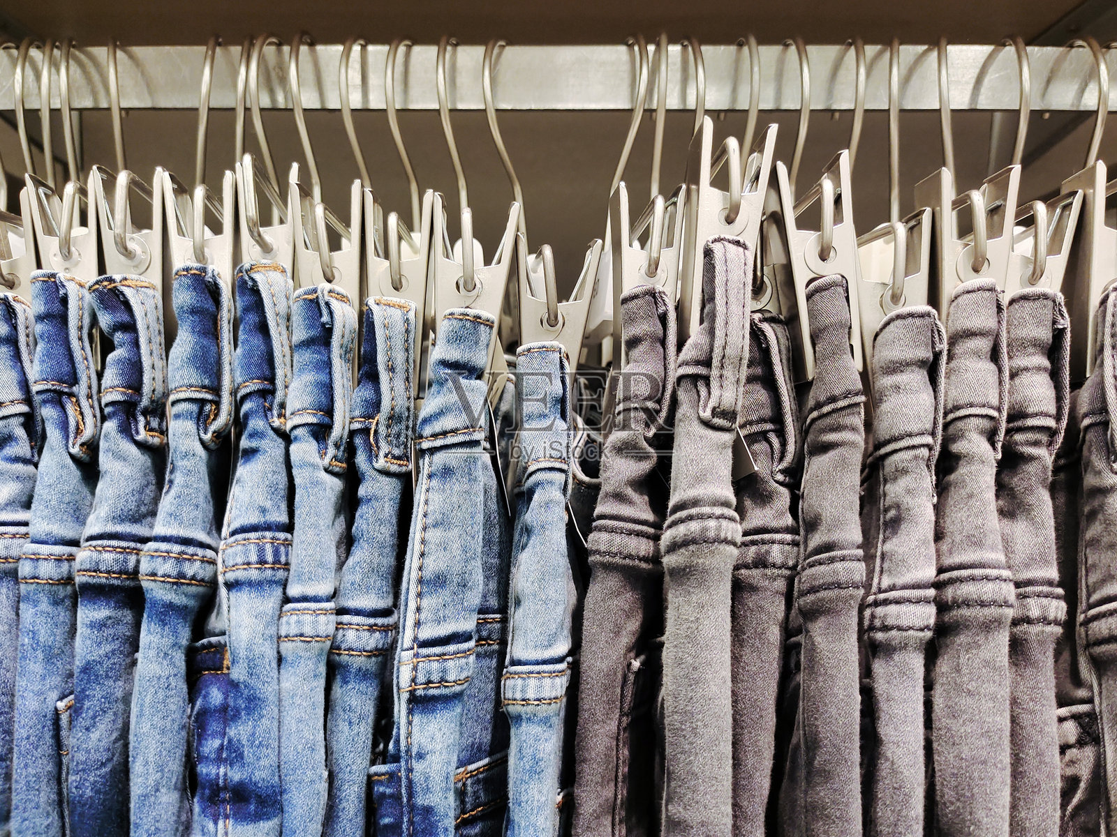 时尚的牛仔裤在服装店中整齐悬挂出售。侧面视图。服装商业销售。照片摄影图片
