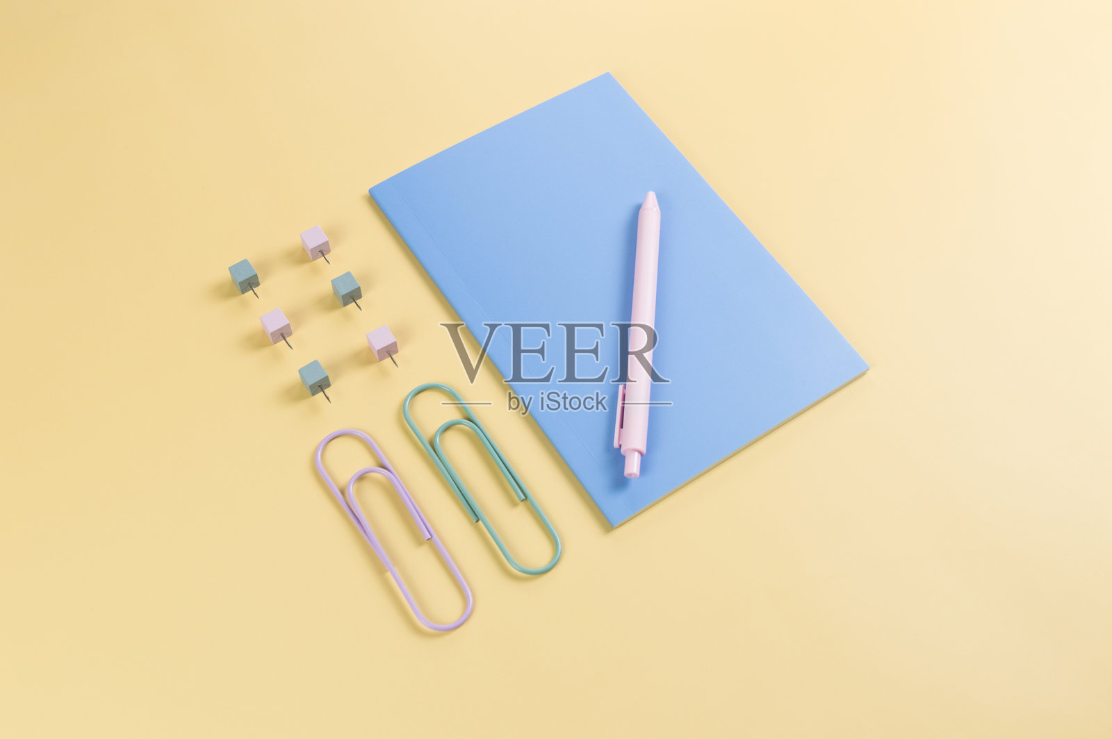 黄色背景上的蓝色笔记本俯视图。回形针、笔和图钉。学校、办公室壁纸。照片摄影图片