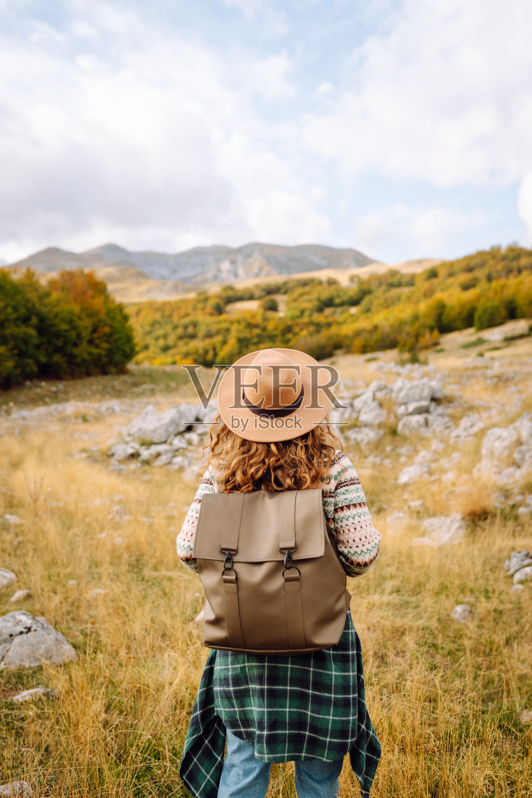 背影。旅行的女性在秋季的开阔田野中探索风景如画的山地景观，远处是起伏的山丘和树木。照片摄影图片