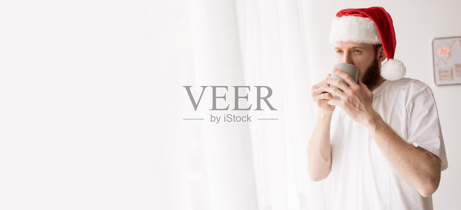 戴着圣诞老人帽的男人在室内窗边喝咖啡照片摄影图片