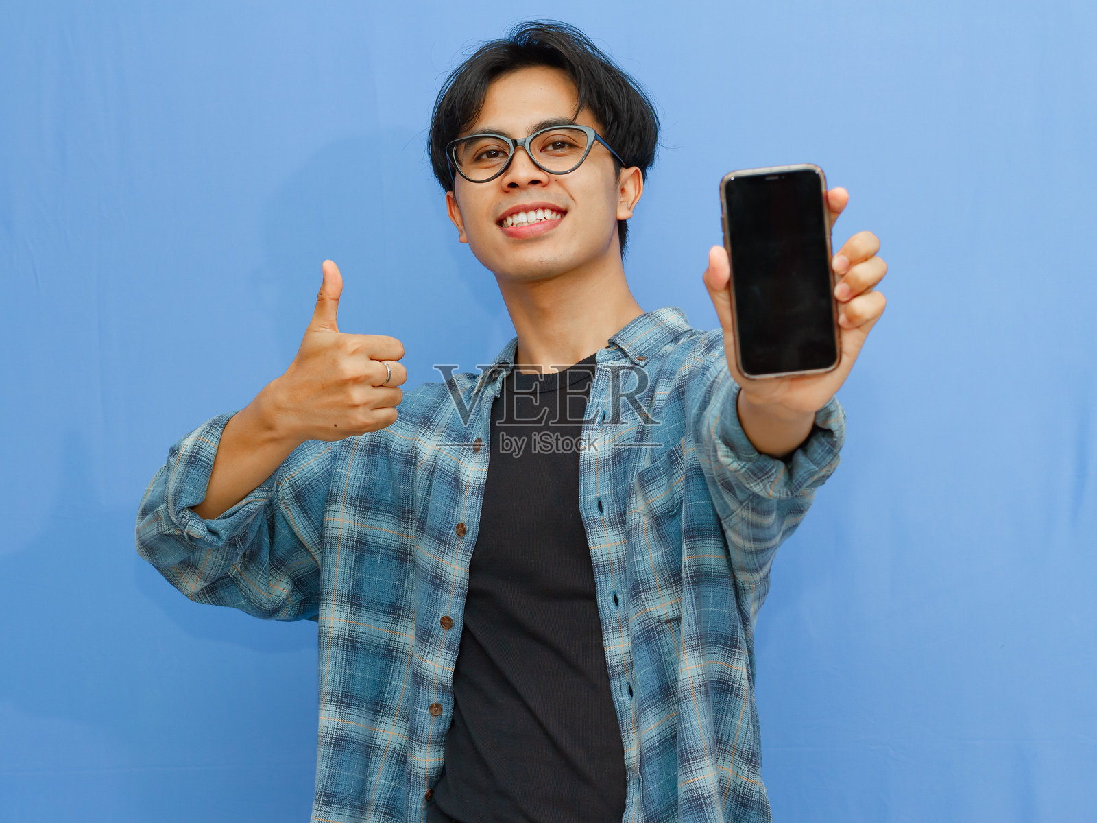 一位快乐的年轻亚洲男子兴奋地展示一块空白的智能手机屏幕，适合广告或宣传内容，背景为蓝色。照片摄影图片