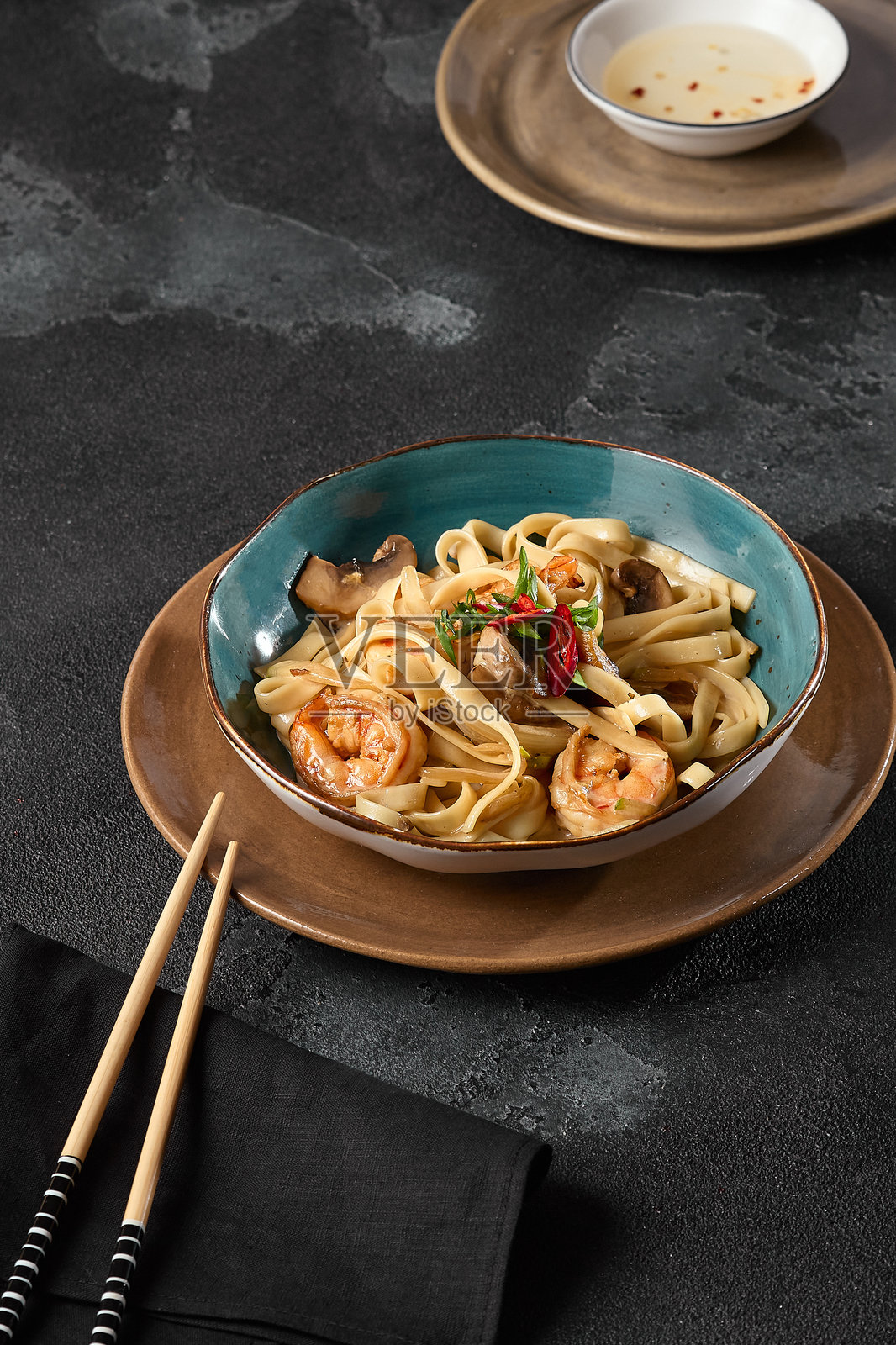优雅陶瓷碗中的虾仁海鲜乌冬面，背景为质朴的深色调照片摄影图片