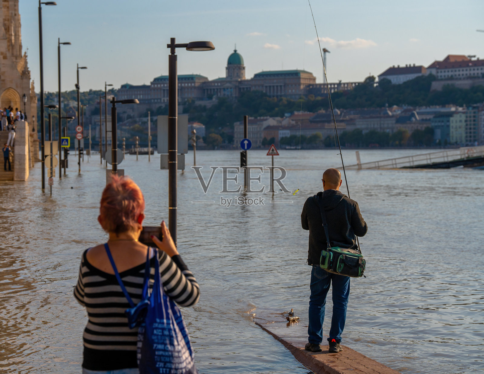 暴风雨“鲍里斯”过后，男子在被洪水淹没的多瑙河中钓鱼，背景是布达佩斯城市和布达城堡照片摄影图片