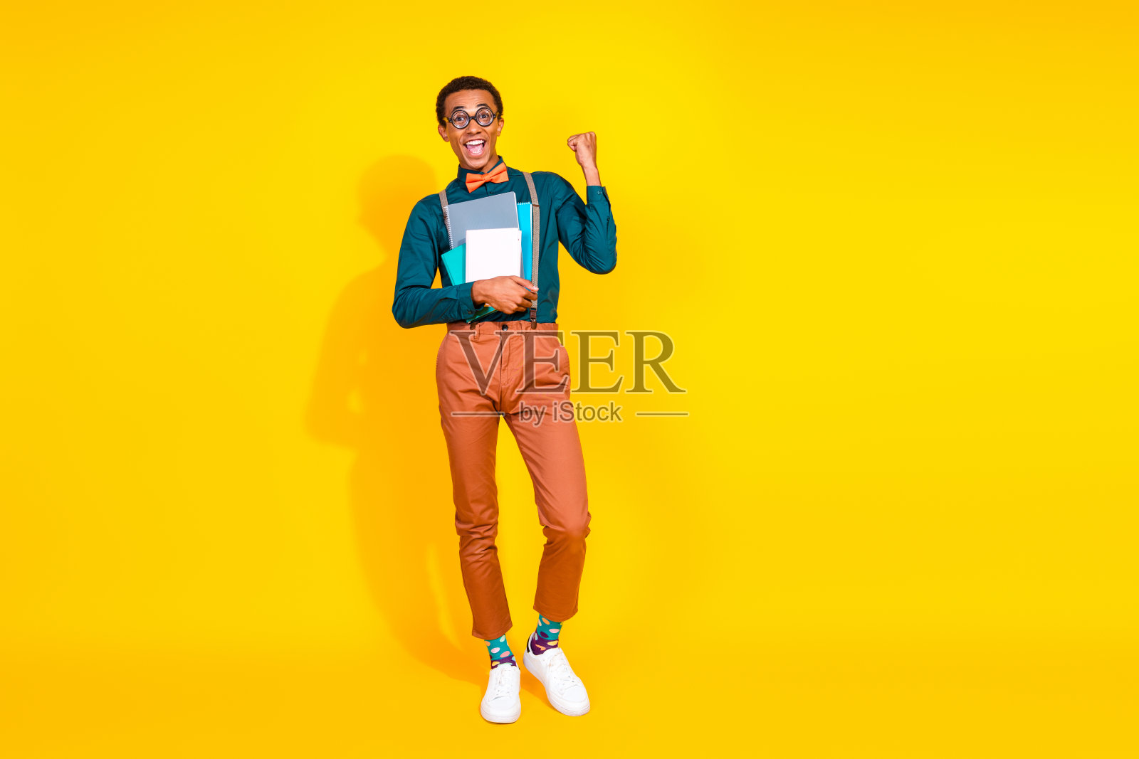 年轻男人黄色背景拿着书本穿着时尚西装举拳获胜全身照照片摄影图片