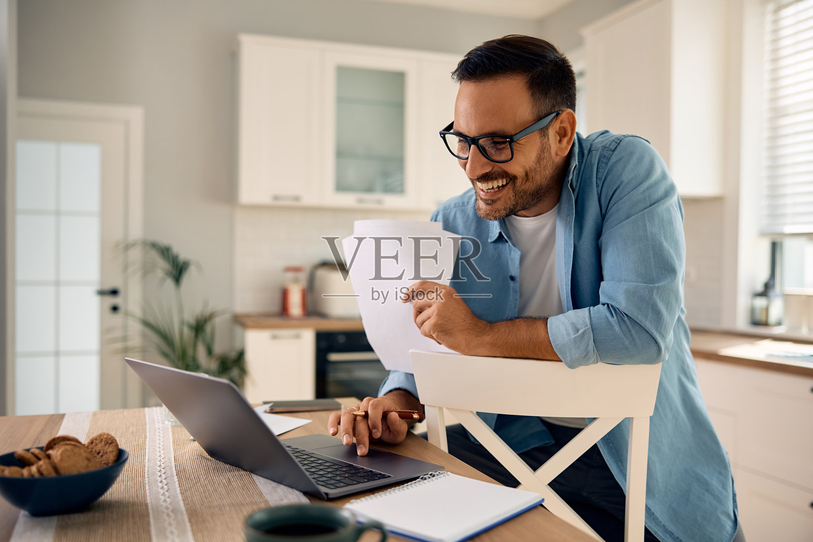 快乐的男人在家中使用电脑分析文件。照片摄影图片