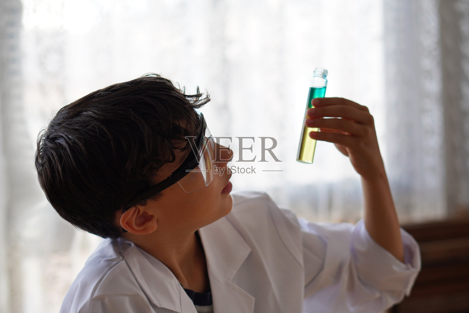 穿着实验服和护目镜的少年男孩，正在进行彩色液体实验照片摄影图片