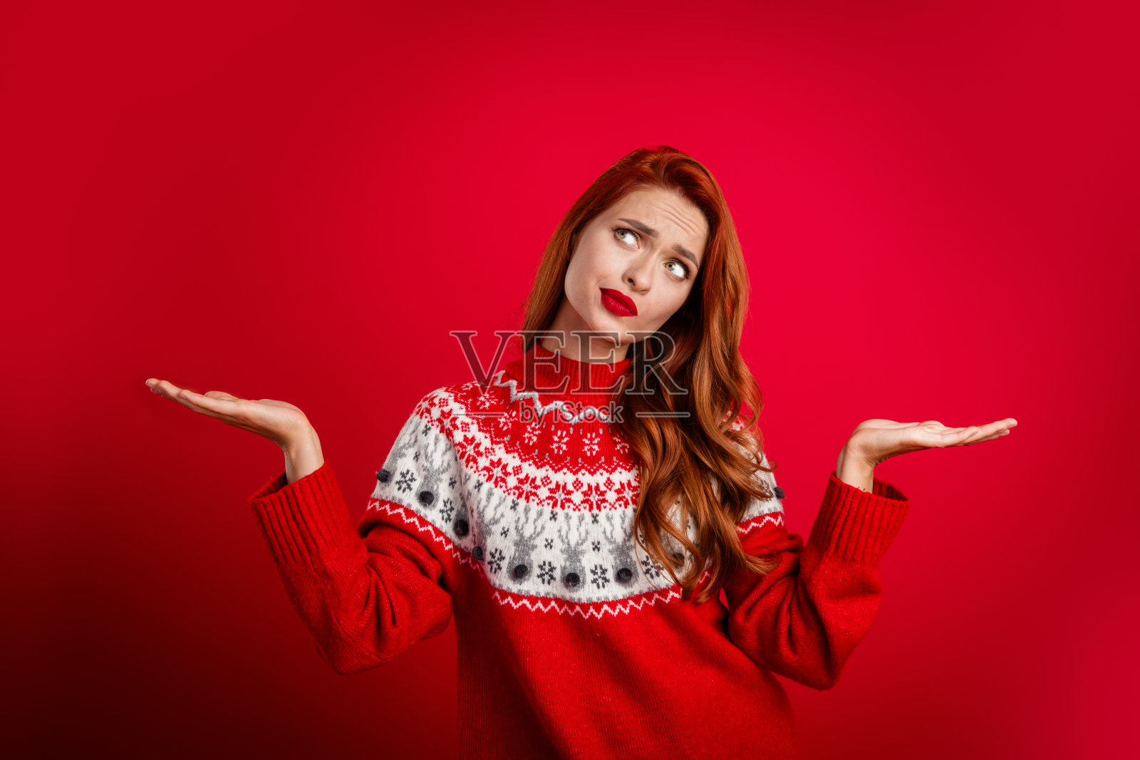 年轻女子身穿圣诞毛衣庆祝节日，在红色背景下保持平衡照片摄影图片