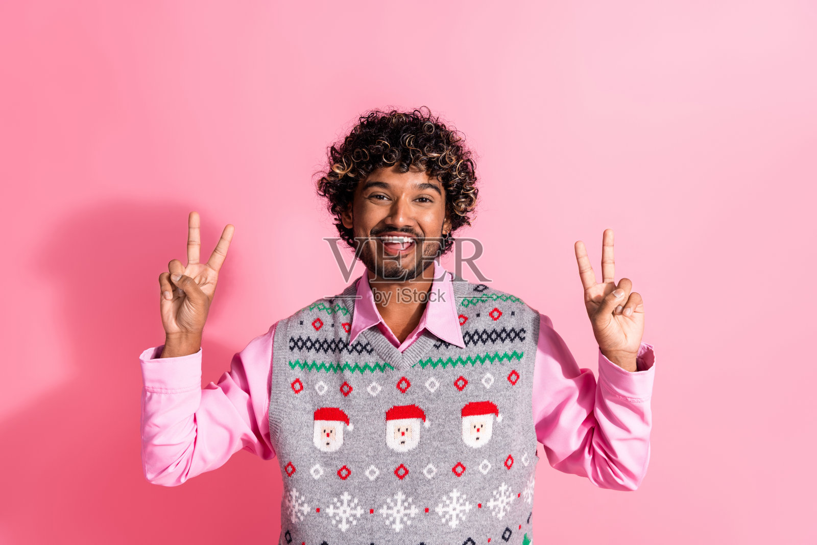 年轻男子圣诞节背心，粉色背景照片，比V手势照片摄影图片