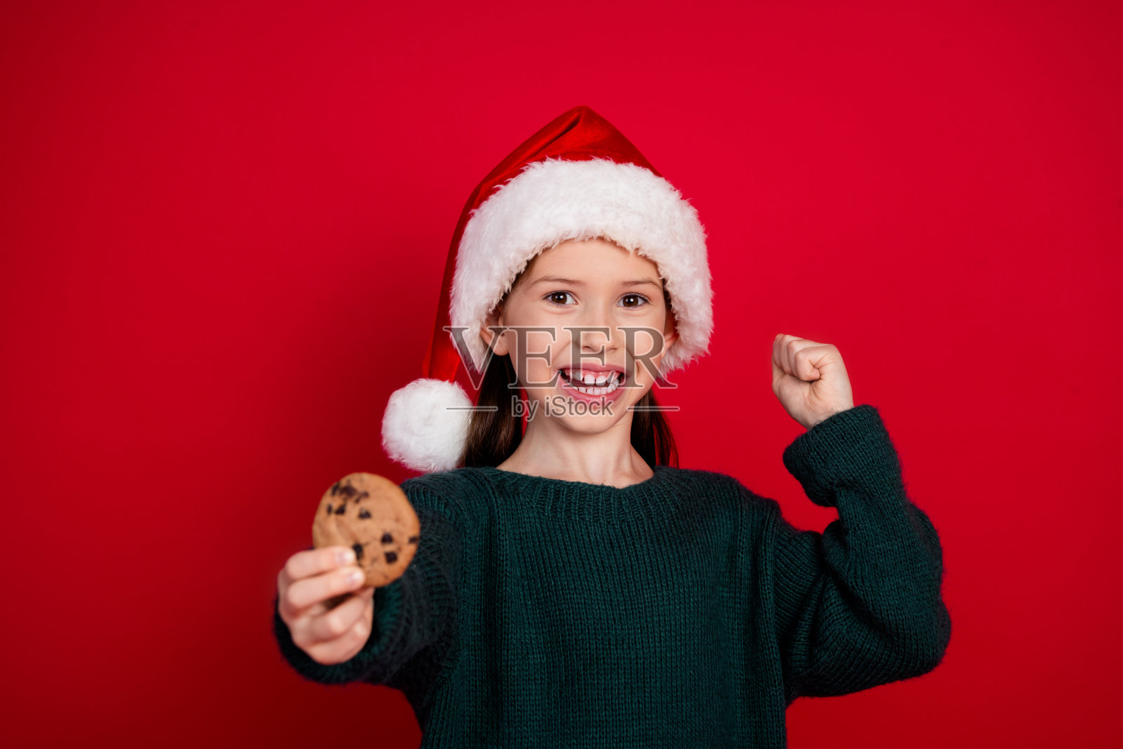 漂亮的小女孩的肖像照，拿着饼干，穿着绿色圣诞主题服装，在红色背景下参加主题派对照片摄影图片