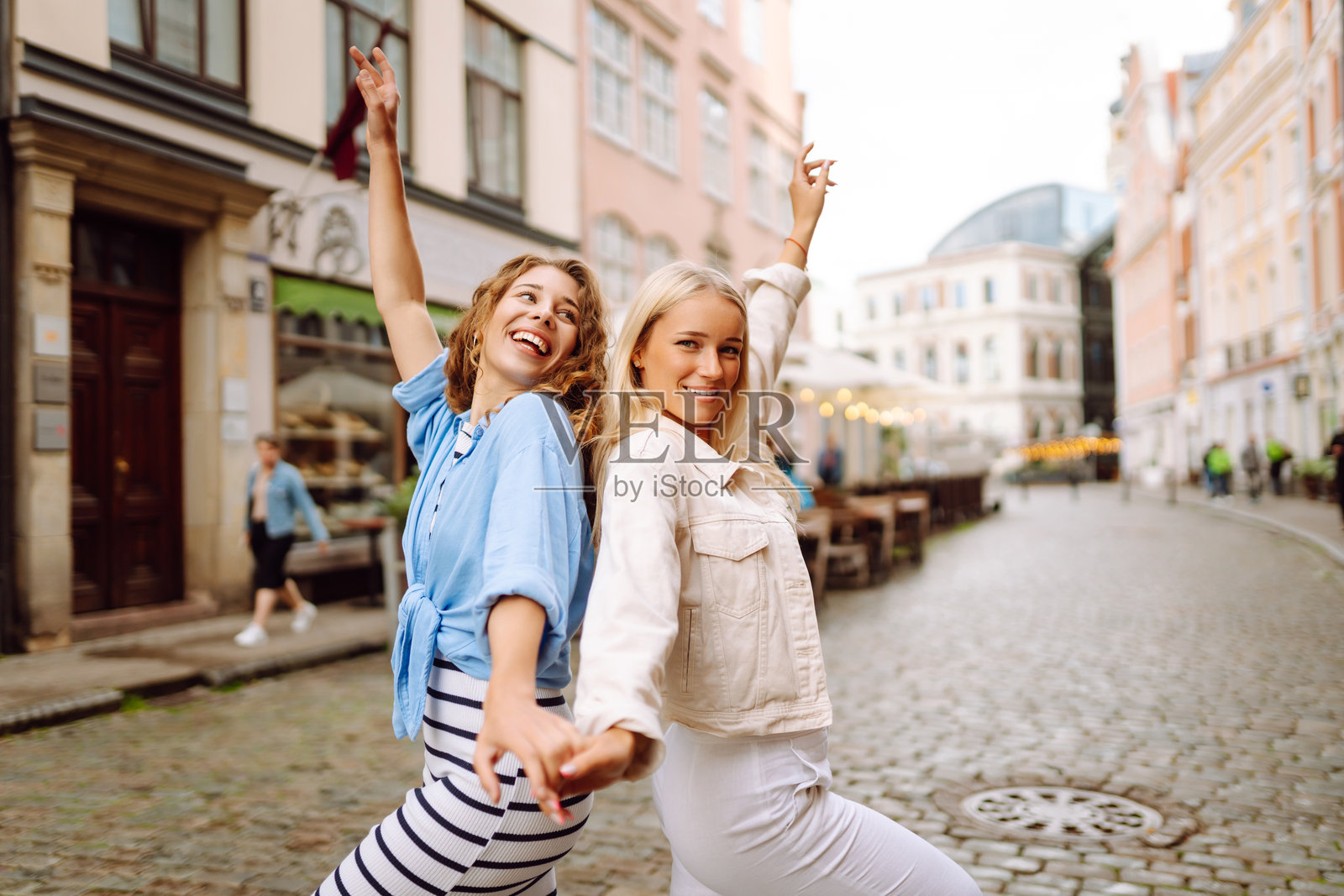 两位女性在阳光明媚的城市广场上欢快地庆祝，展现了友谊和快乐。照片摄影图片