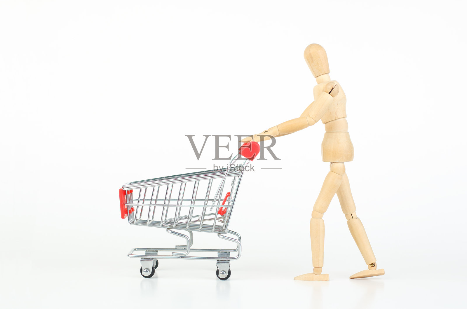 木质人形模特推着购物车，背景为白色。照片摄影图片