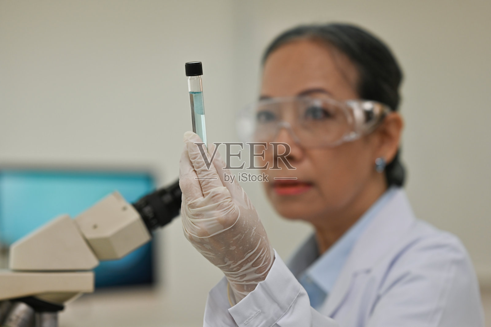 在实验室工作的年长的亚洲女科学家，正在观察样本，焦点集中在拿着试管的手上照片摄影图片