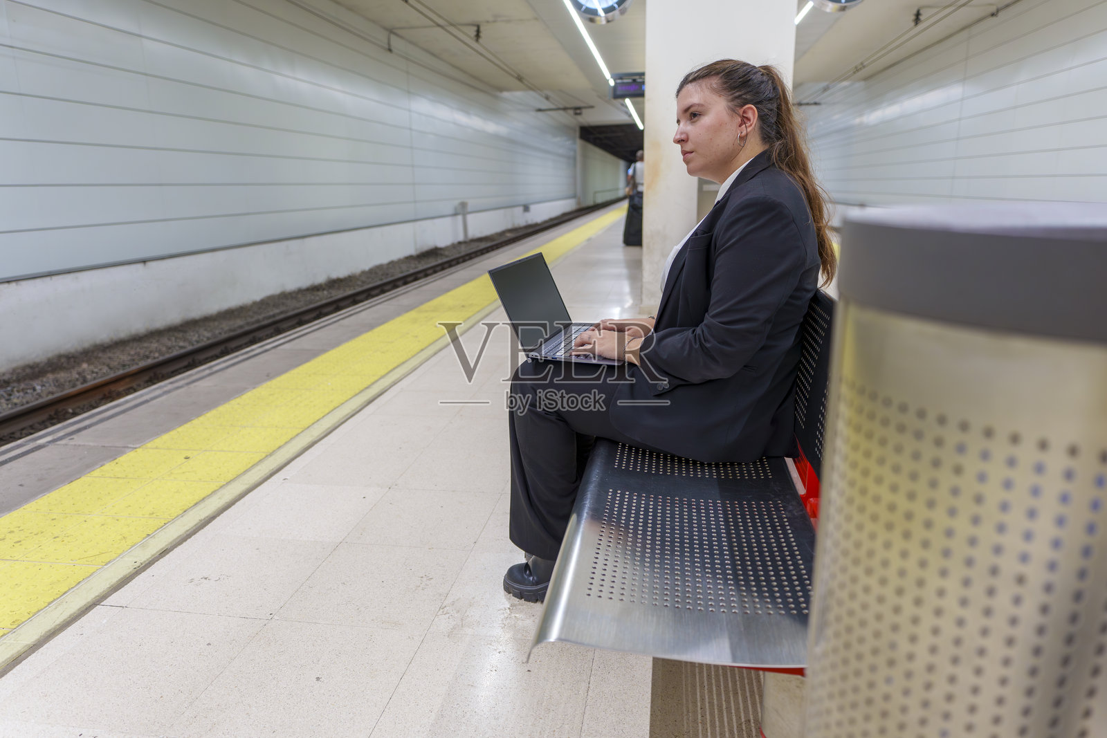 年轻女性穿着商务套装在火车站候车平台上使用笔记本电脑工作照片摄影图片