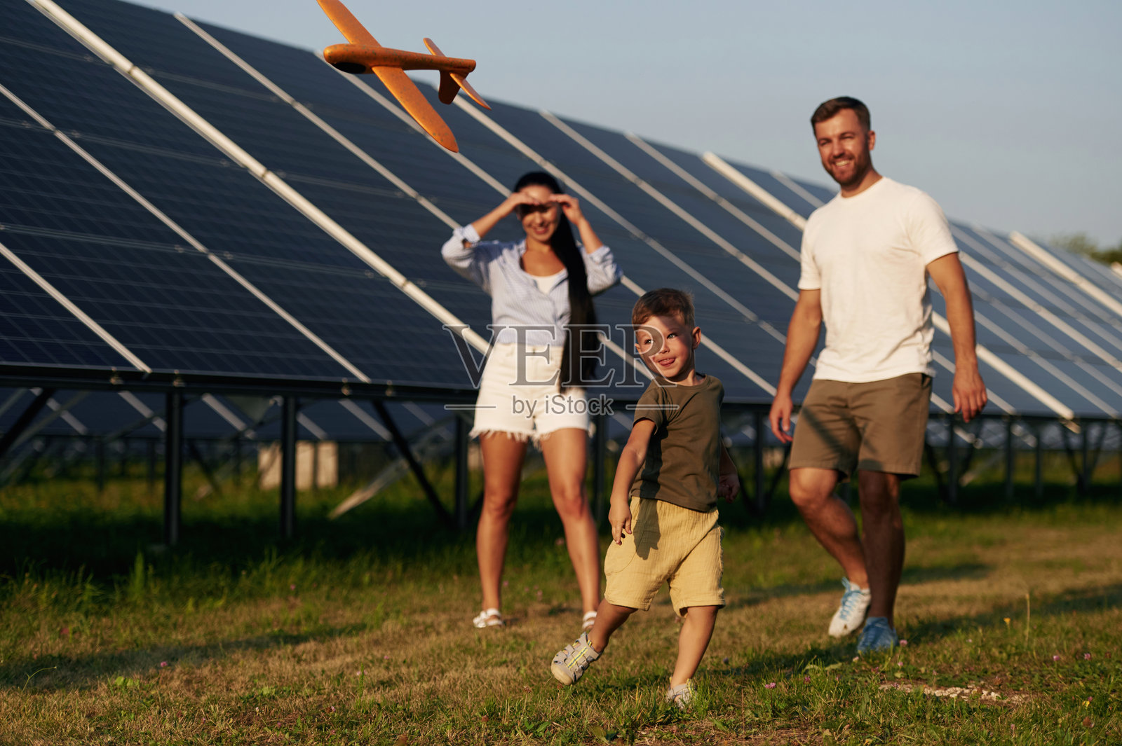 积极跑步，拿着玩具飞机。父亲、母亲和小儿子在太阳能电池板附近户外活动照片摄影图片