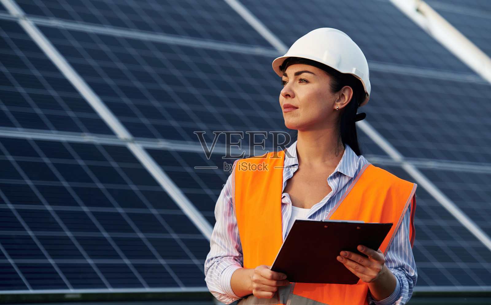 手中的笔记本。穿制服的女工程师在太阳能电池板附近照片摄影图片