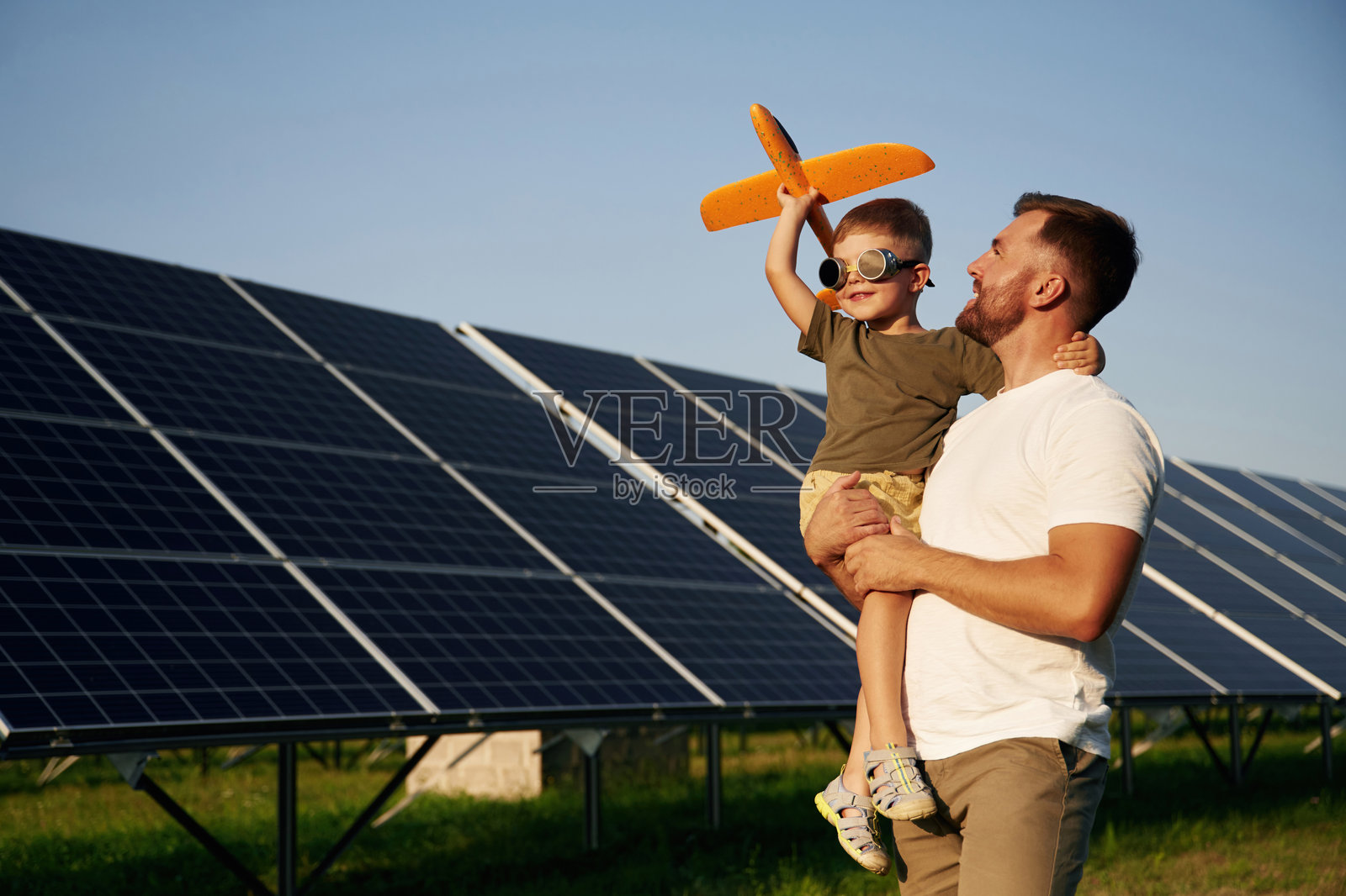 飞行员眼镜和玩具飞机：父亲和儿子在太阳能电池板旁照片摄影图片