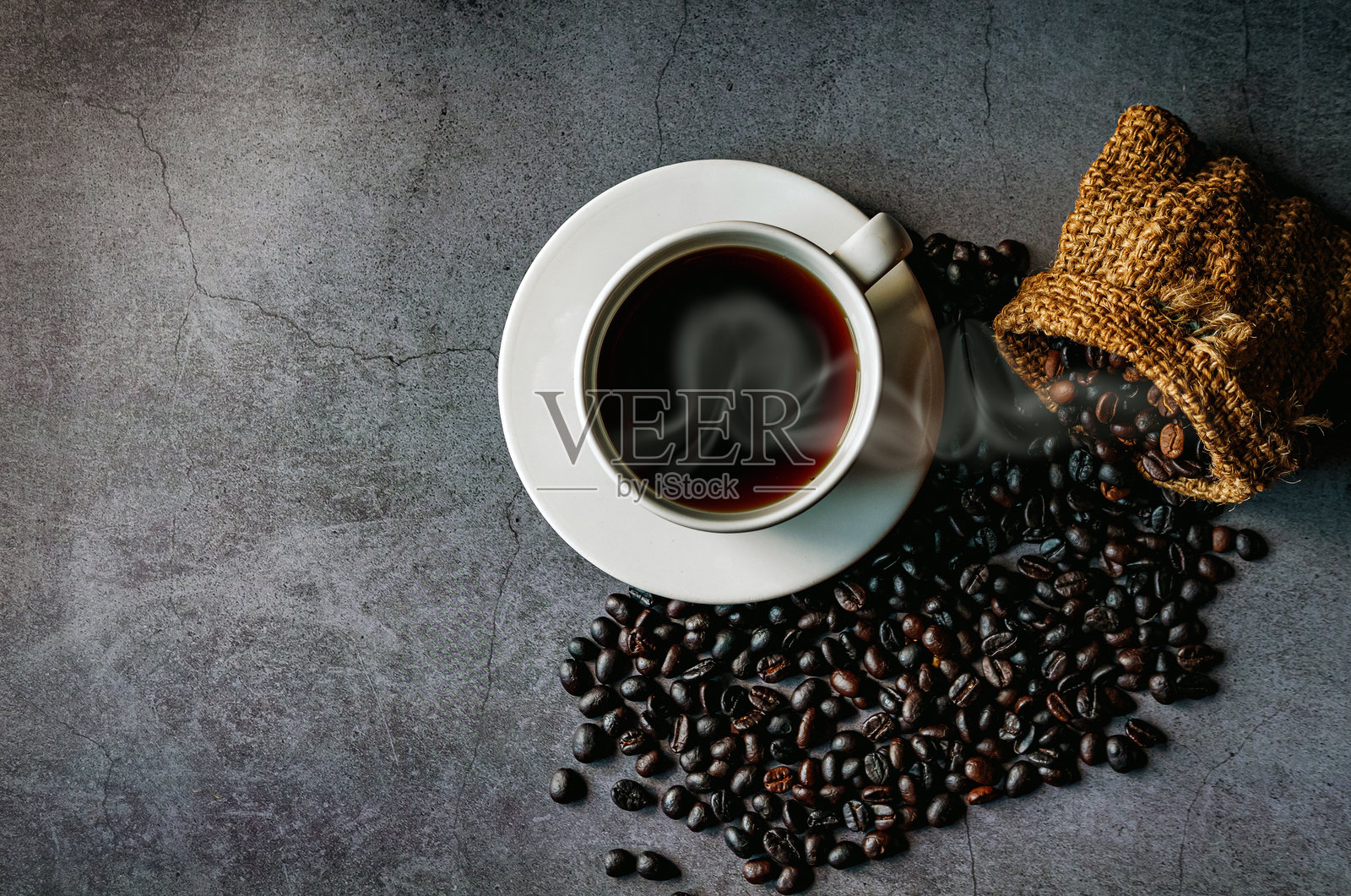 美式咖啡杯和烘焙咖啡豆从麻袋中掉落在灰色背景上，黑色咖啡杯散发香气，俯视图照片摄影图片