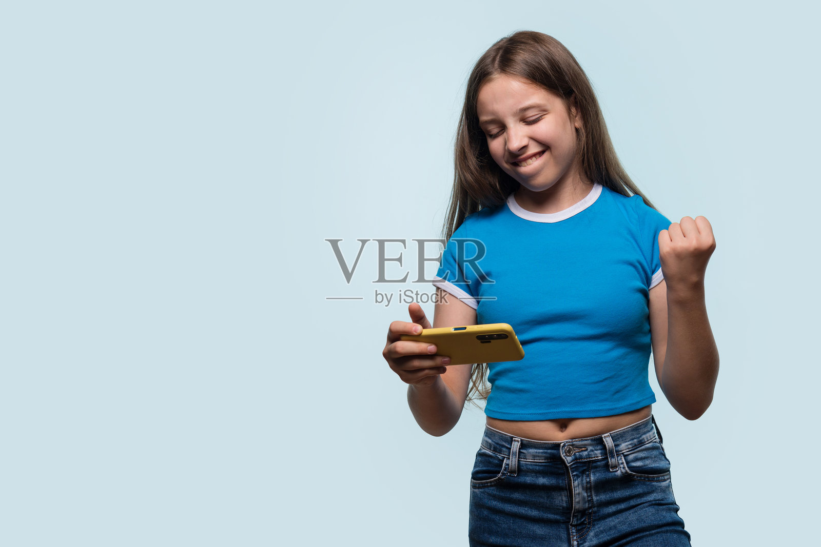 女孩握紧拳头，得意地看着智能手机。照片摄影图片