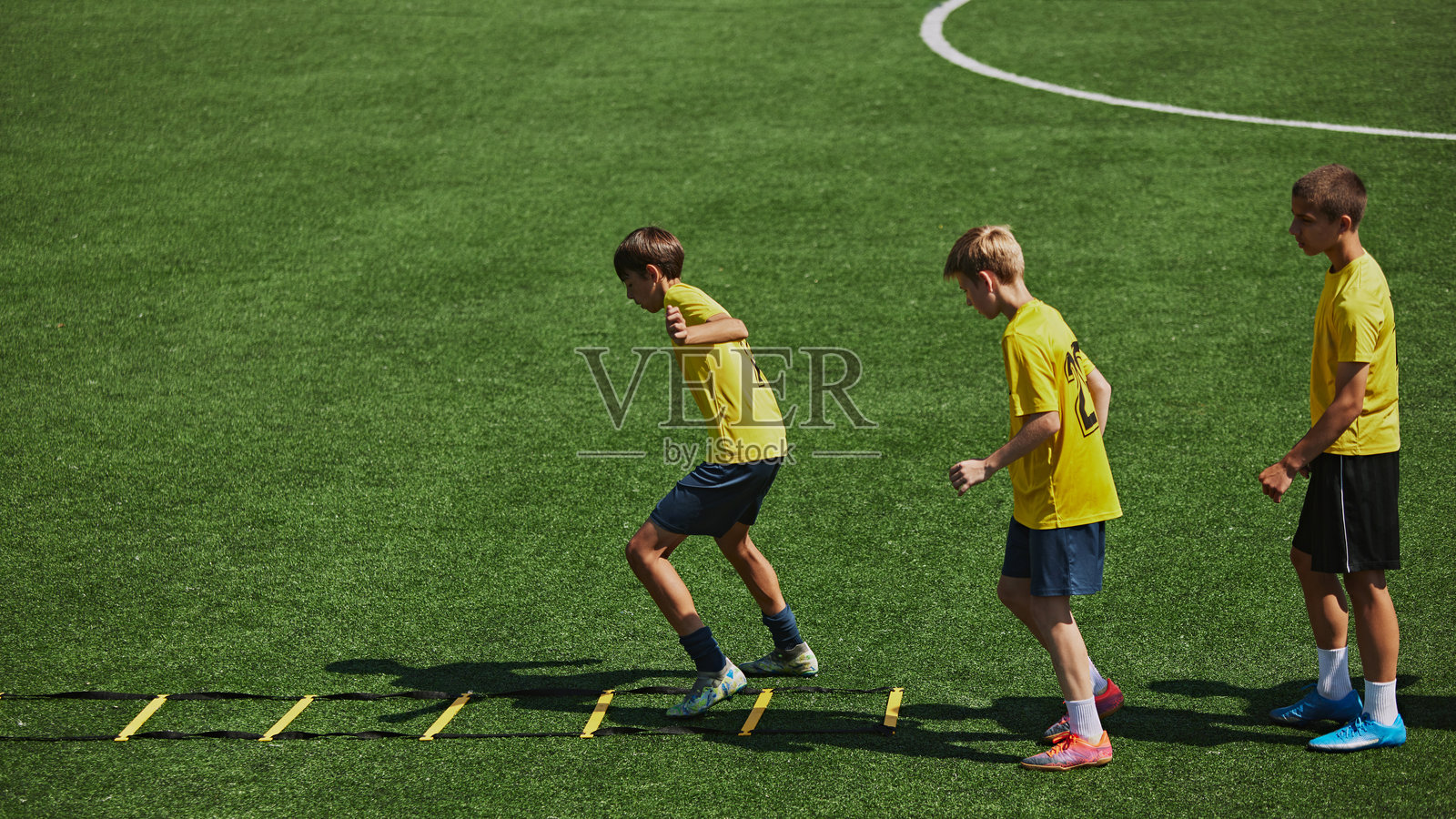 在户外足球场训练的男孩：练习灵敏梯上的步法照片摄影图片