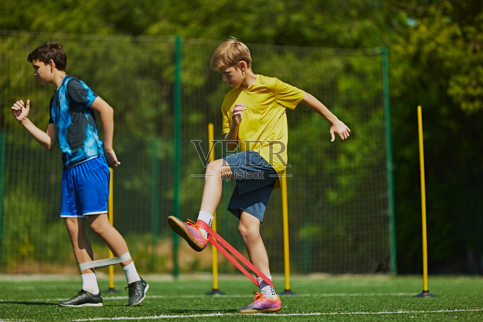 两个男孩穿着运动服在户外足球场训练，赛前用弹力带热身照片摄影图片