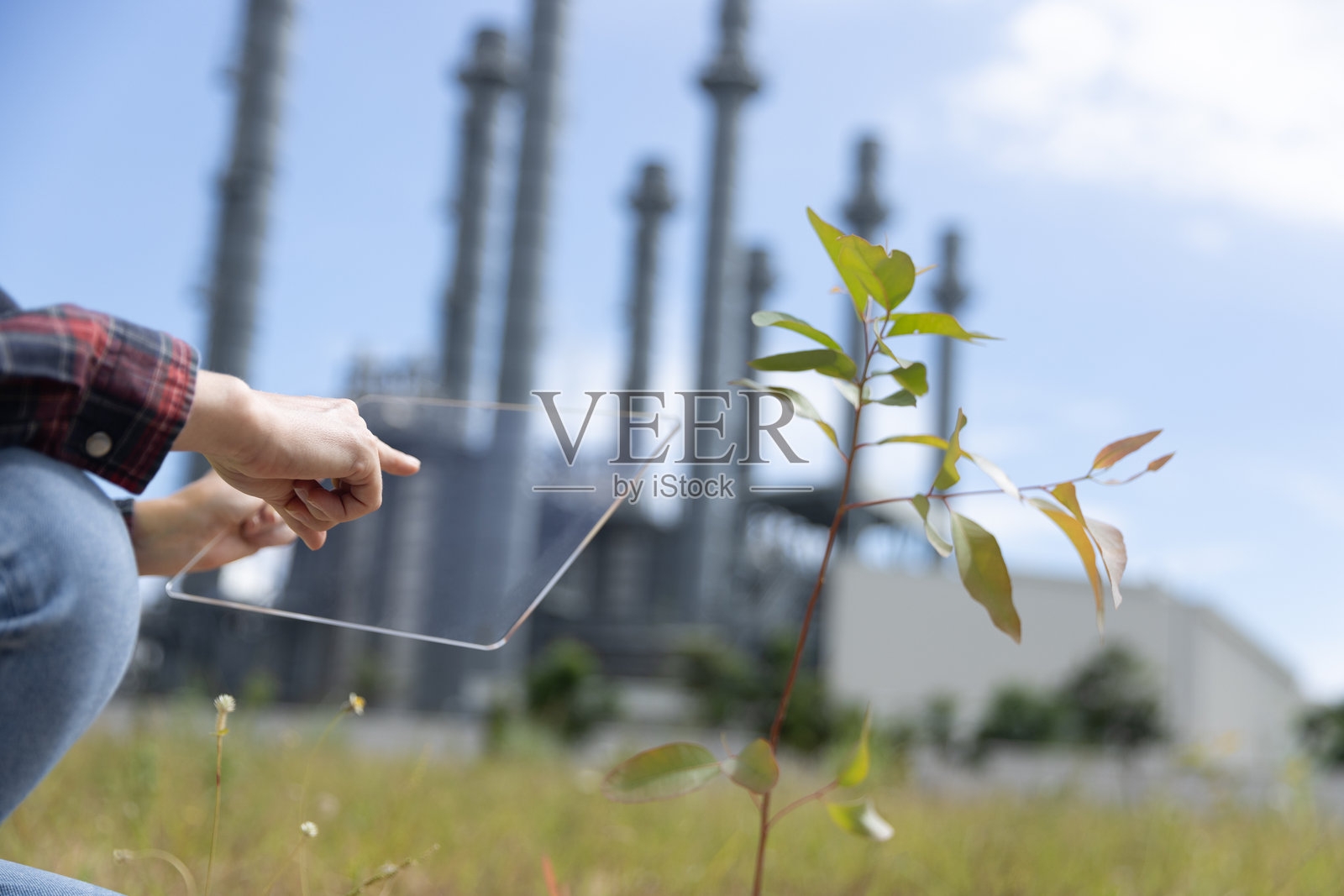 一位聪明的女性项目负责人正在手动种植可再生资源树木，以减少污染，手中展示环境、社会和可持续商业治理的ESG图标，旁边是一座火力发电厂。照片摄影图片