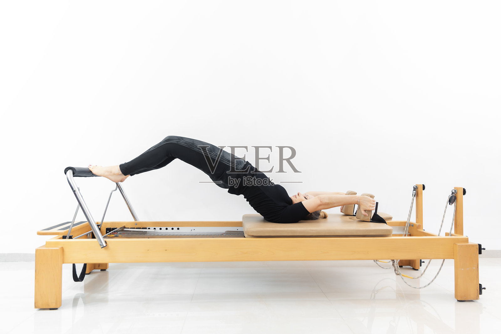 穿着黑色运动服的运动型女人在普拉提塑形机半圆上训练照片摄影图片