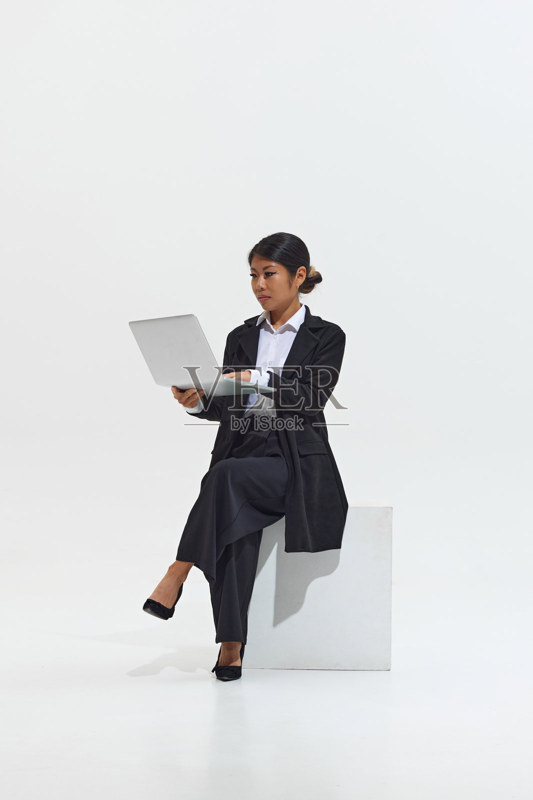 身穿黑色职业装的年轻亚洲女性坐在笔记本电脑前，看起来专注地工作照片摄影图片