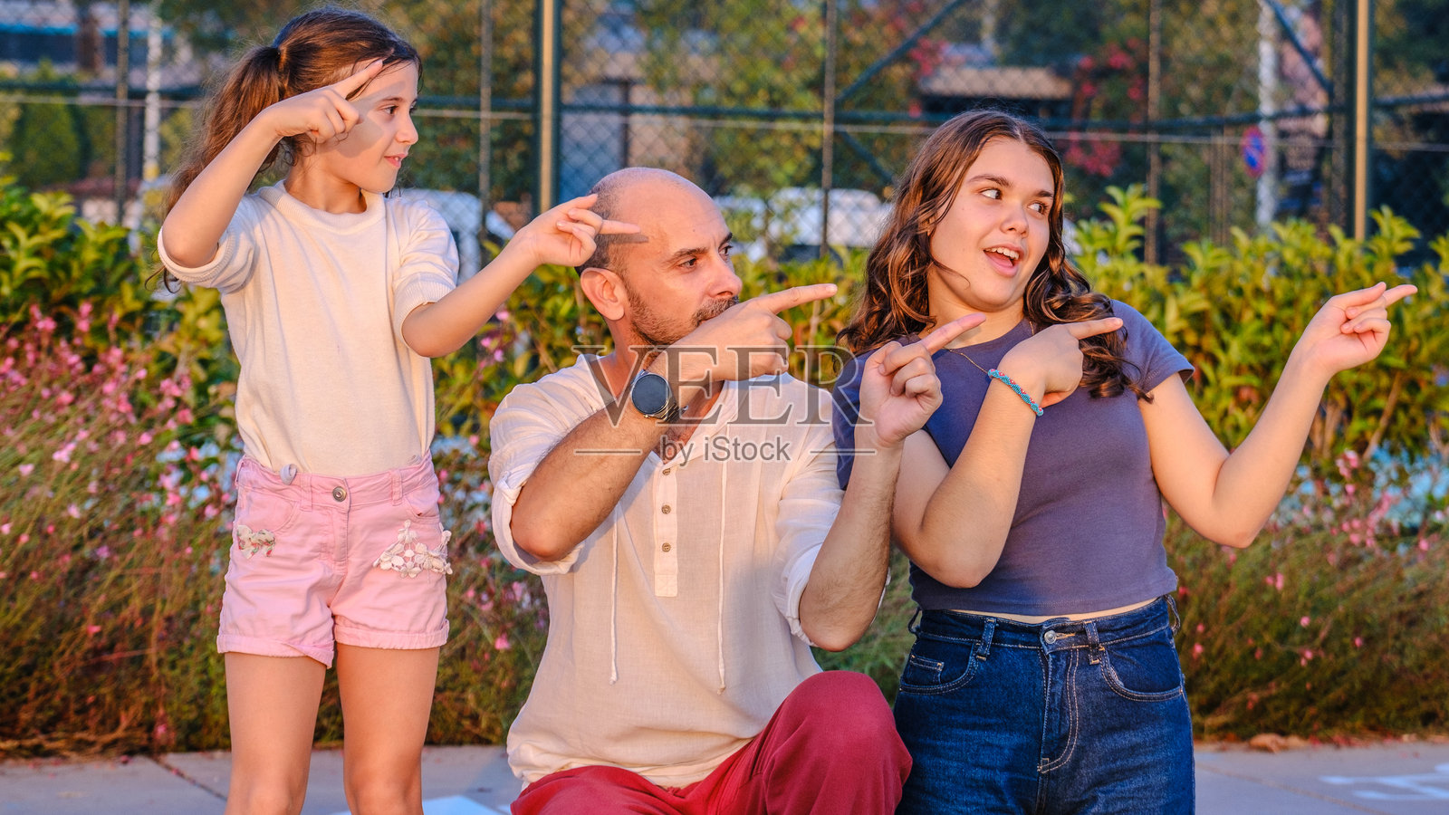 一位中年父亲与他的女儿们一起在树林公园的傍晚，手指指向特定的地方，面向镜头。照片摄影图片