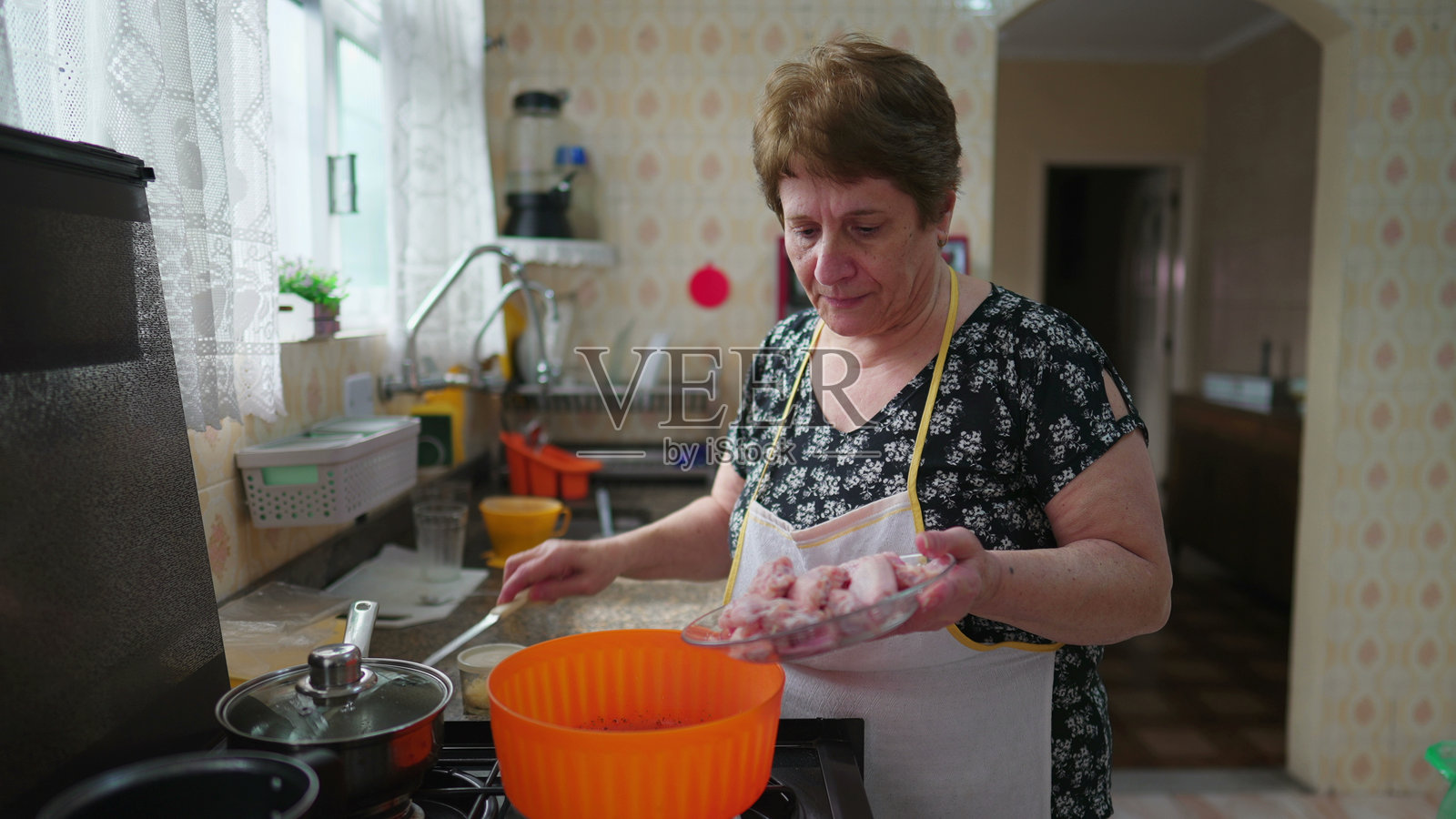 年长女性在真实的家庭生活场景中烹饪。老年人将鸡肉放入碗中准备餐点。照片摄影图片