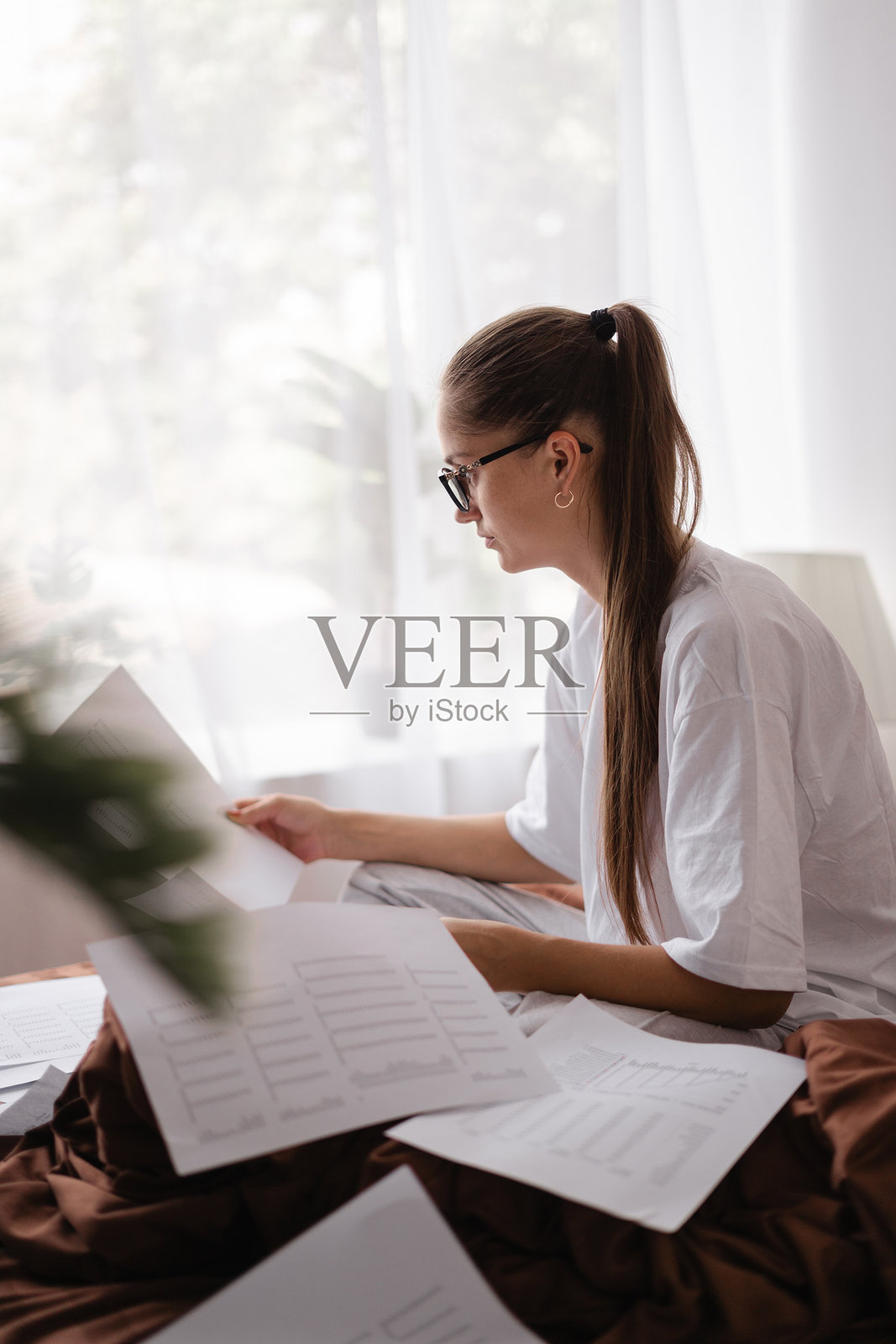 忙碌的女人在家中卧室的床上处理纸质文件，进行会计记账照片摄影图片