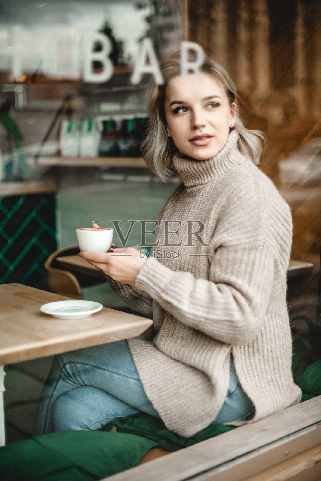 一位女性坐在咖啡馆的桌子旁，手里拿着一杯咖啡。照片摄影图片