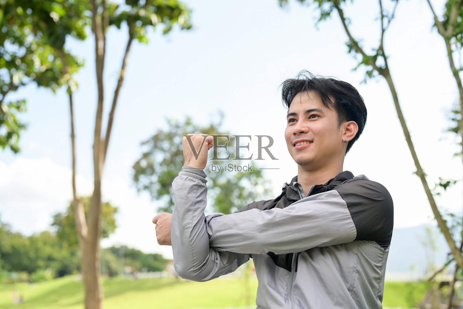 一位英俊、健壮的亚洲男子穿着运动服，在公园里伸展手臂，热身准备慢跑。照片摄影图片