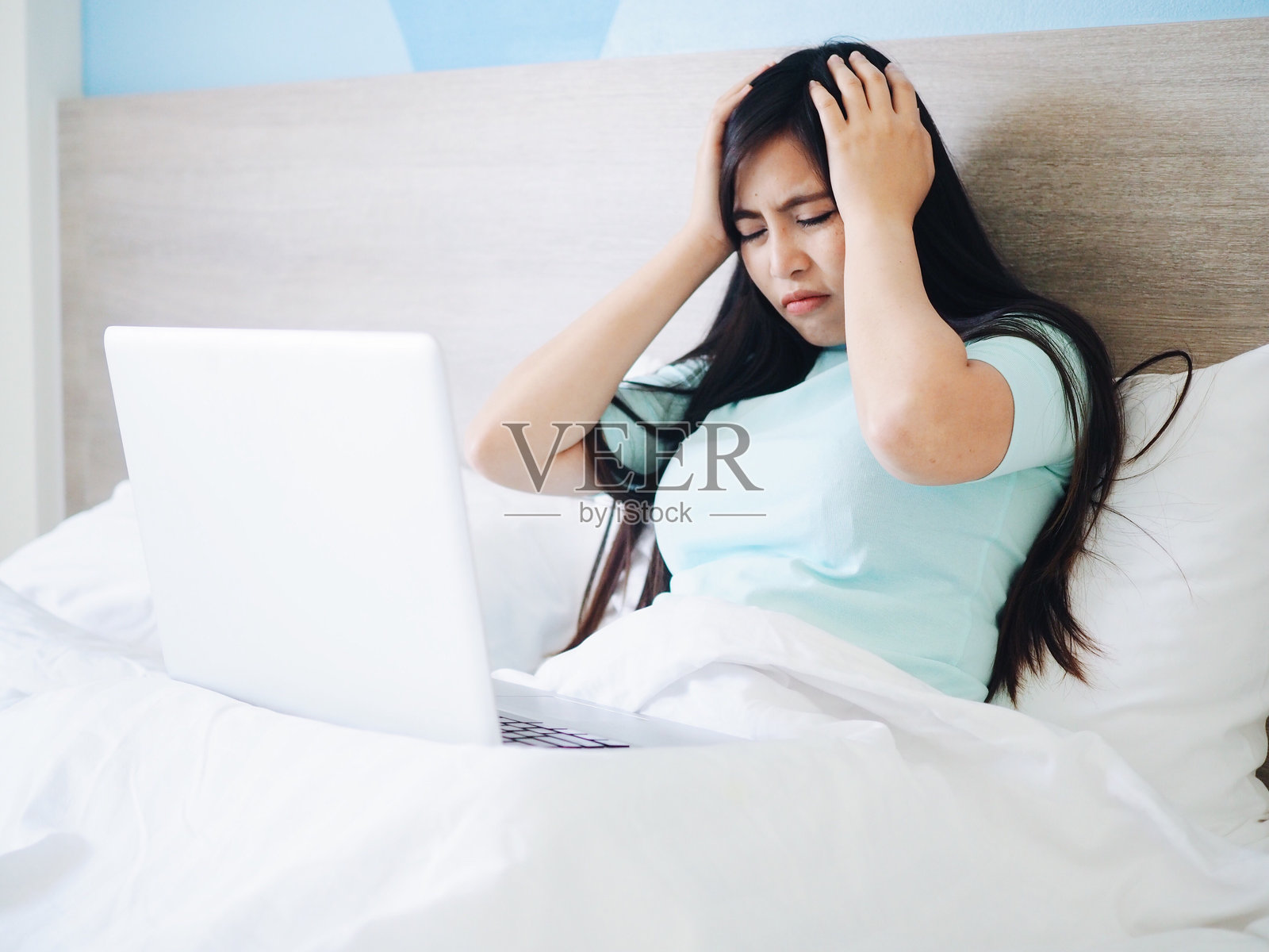年轻女性在家床上用笔记本电脑工作，感到头痛照片摄影图片