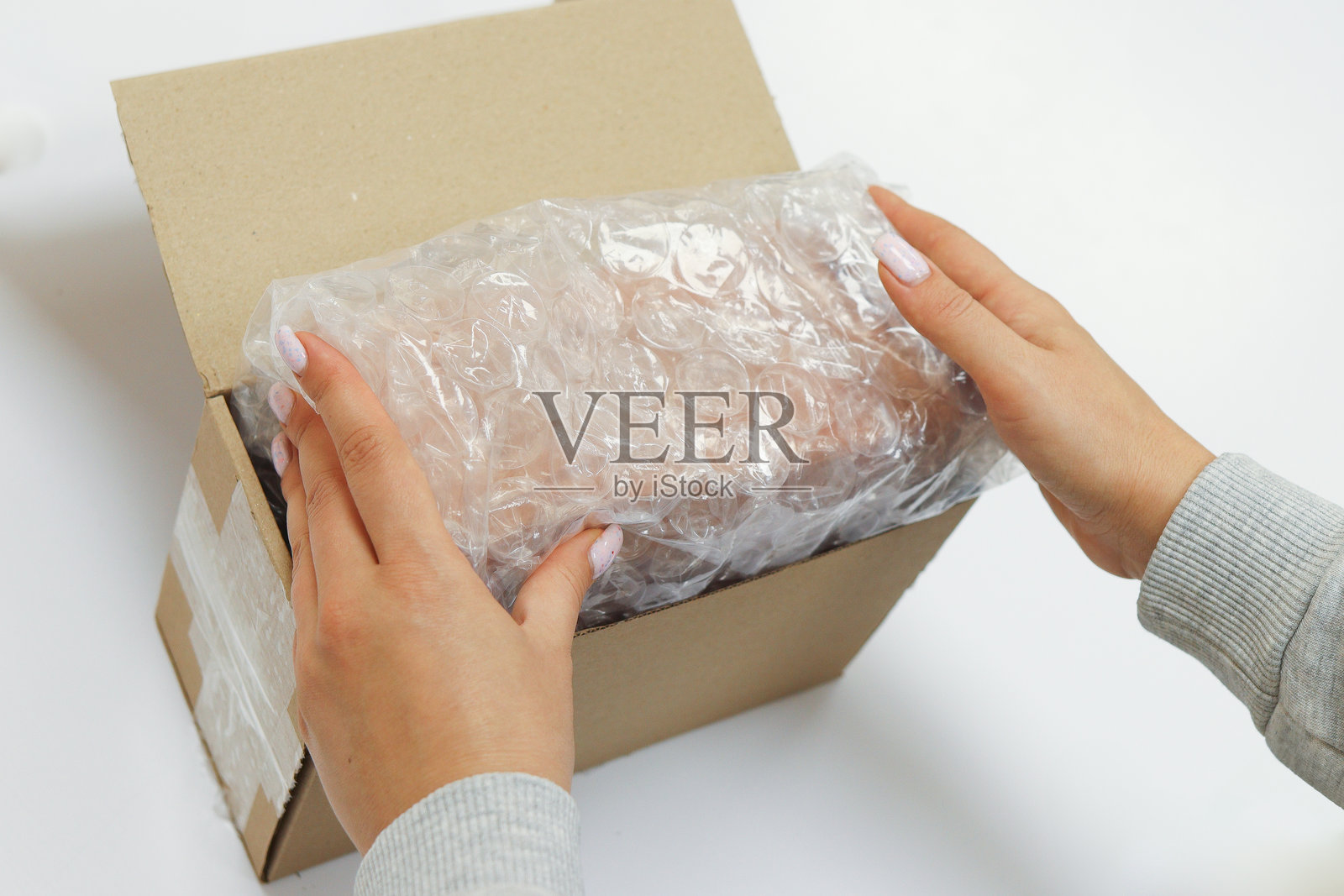 女性的手正在用气泡膜包装产品以保护包裹，并放入一个棕色纸箱中，正在拆包裹。照片摄影图片