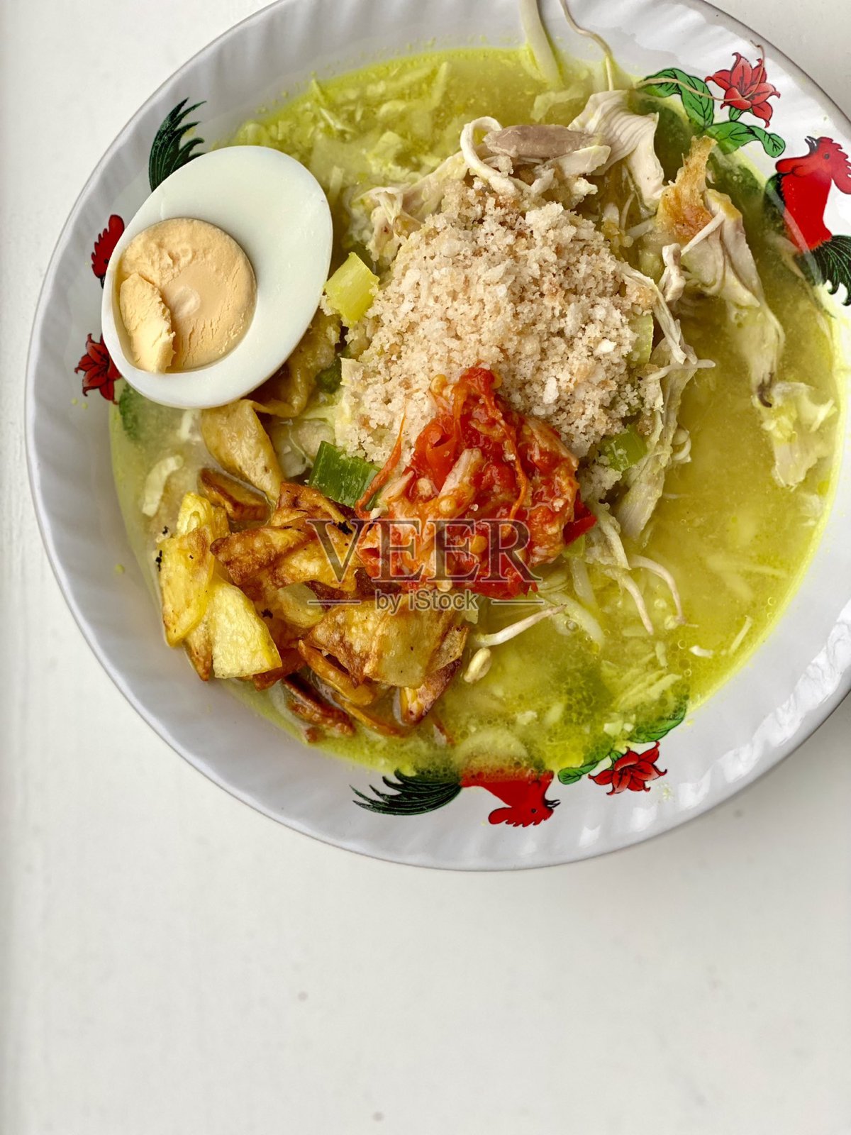 印尼传统鸡肉汤（soto ayam）主要由清汤、姜黄、鸡肉和蔬菜组成。配有煮鸡蛋、青柠和炸葱。选定焦点。照片摄影图片
