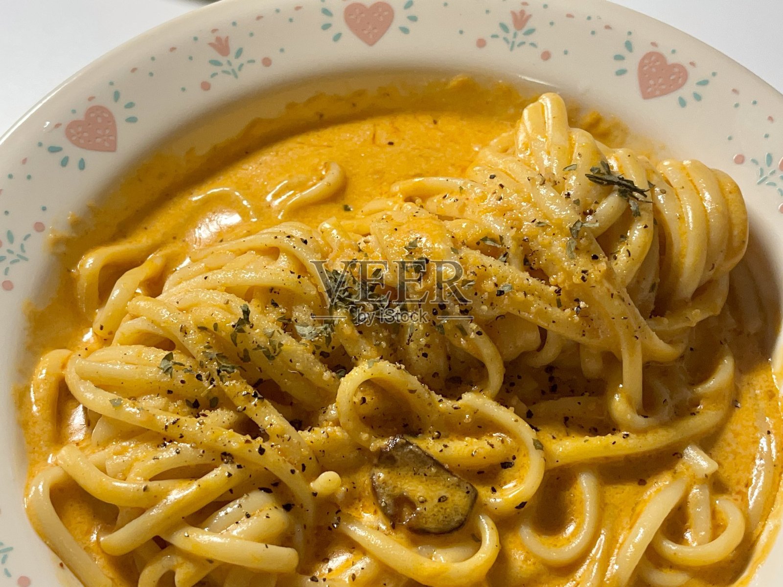 意大利肉酱面上撒有罗勒，旁边有奶酪和水，放在红色餐巾和白色木质桌面上。照片摄影图片