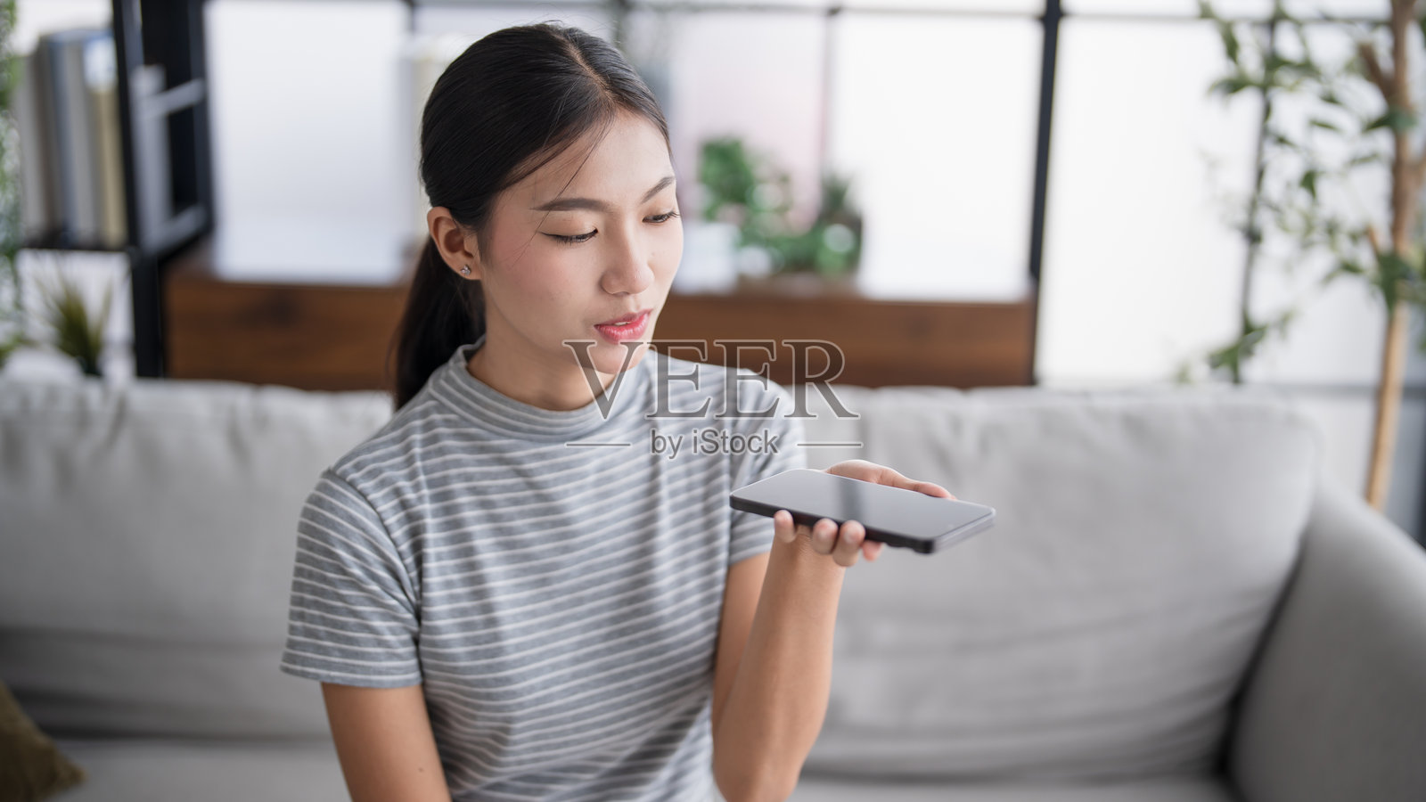 亚洲女性在家中使用智能手机与在线助手进行语音助手对话 语音聊天机器人对话式人工智能 现代科技。照片摄影图片