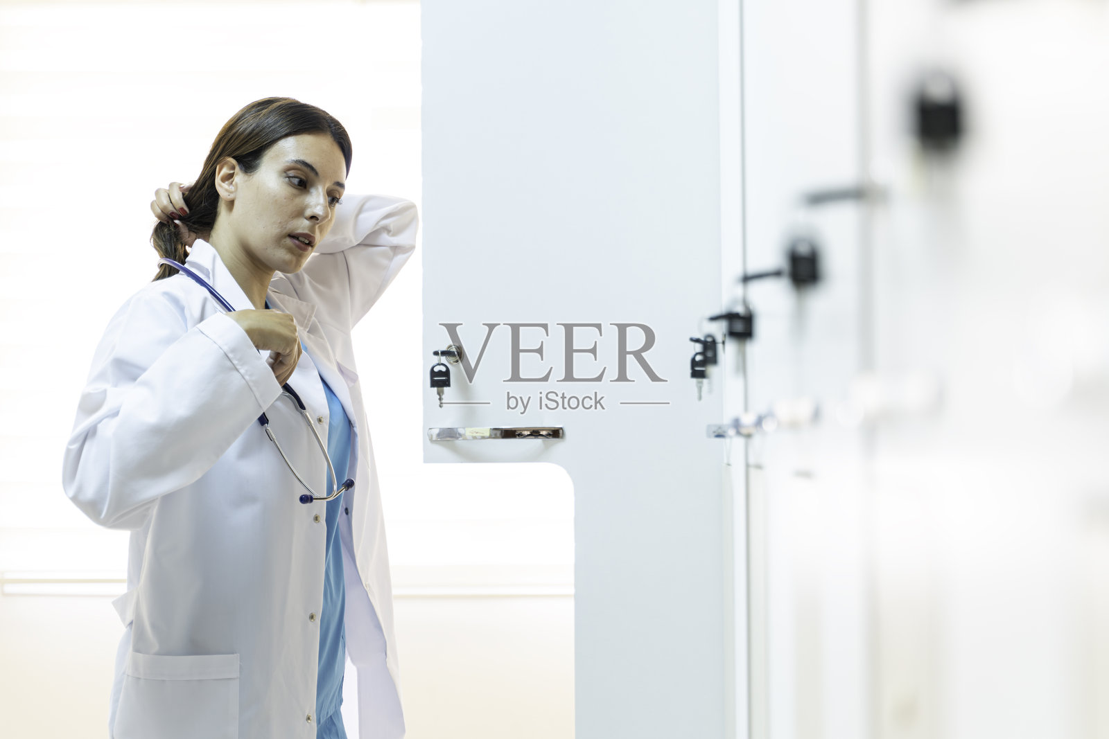 年轻女医生在更衣室里把衣服放进储物柜。照片摄影图片