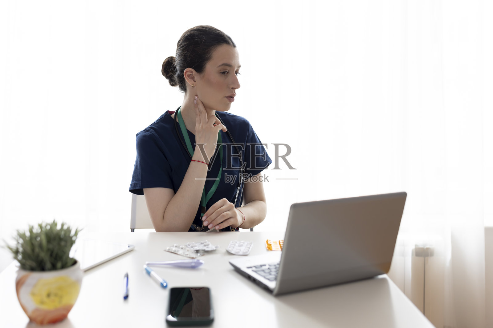 一位迷人的女医生微笑着看向镜头，展示如何检查脉搏，同时在咨询室使用笔记本电脑。照片摄影图片