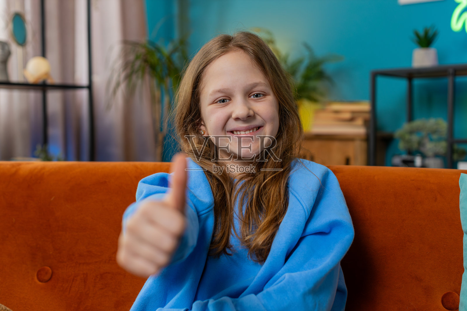 快乐的小女孩对着镜头竖起大拇指，表示赞同，像是传递积极的信号，带来好消息。照片摄影图片