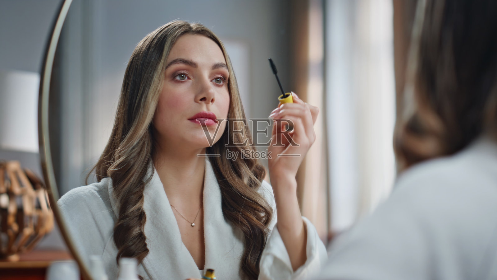 浴室里的女人在镜子前涂抹睫毛膏。照片摄影图片