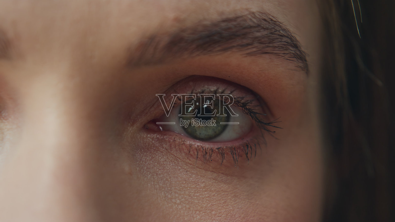 宏观镜头下的女性眼睛注视着摄像机，正在工作室中拍摄。女孩的绿色眼睛在眨动。照片摄影图片