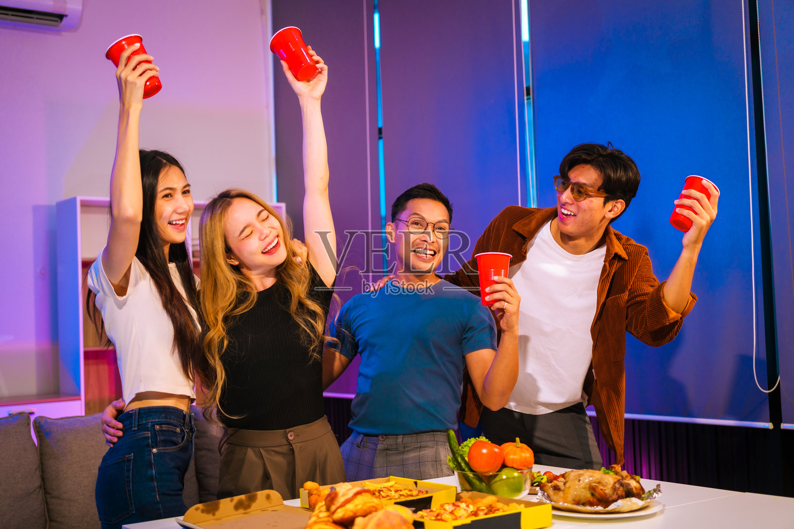 四位亚洲朋友，两男两女，在办公室派对上庆祝。他们享受着美食、饮料和欢笑，因团队合作和友谊而更加亲密。照片摄影图片