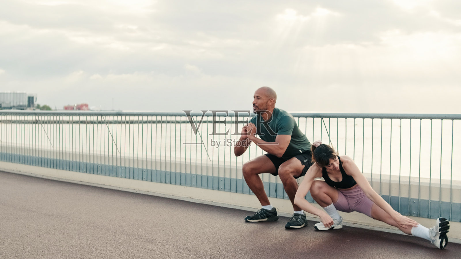 强壮的男性运动员在深蹲，女性在做拉伸。一起保持良好的身材。情侣的动力，享受团队合作，情侣目标。照片摄影图片
