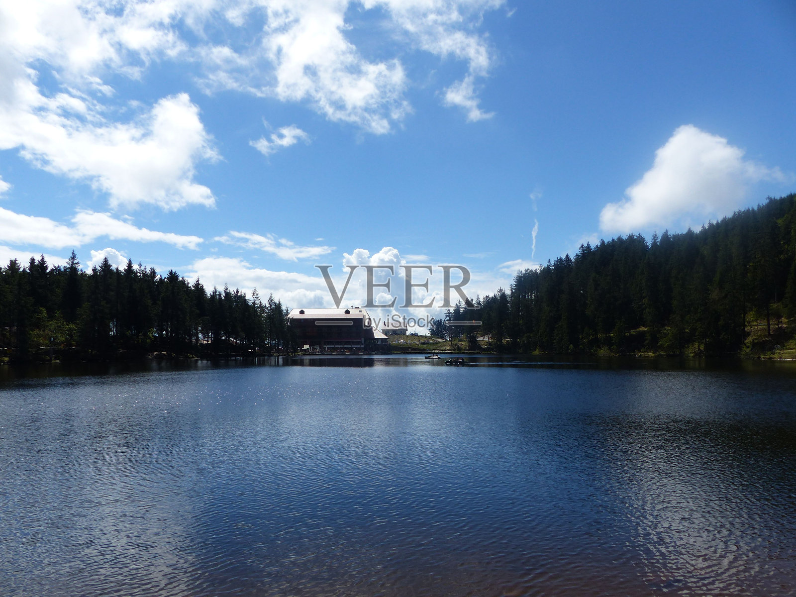 德国穆姆尔湖上空晴朗的蓝天和白云，森林中有一座房子。照片摄影图片