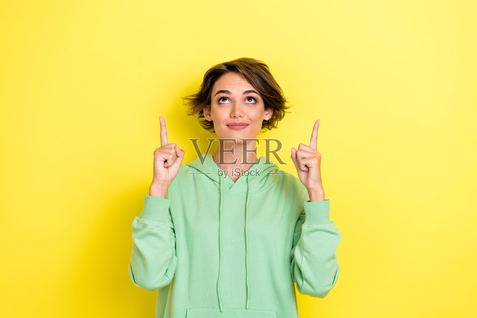 可爱的年轻女士的照片肖像，指着空旷的空间，穿着时尚的绿色衣服，背景为黄色。照片摄影图片